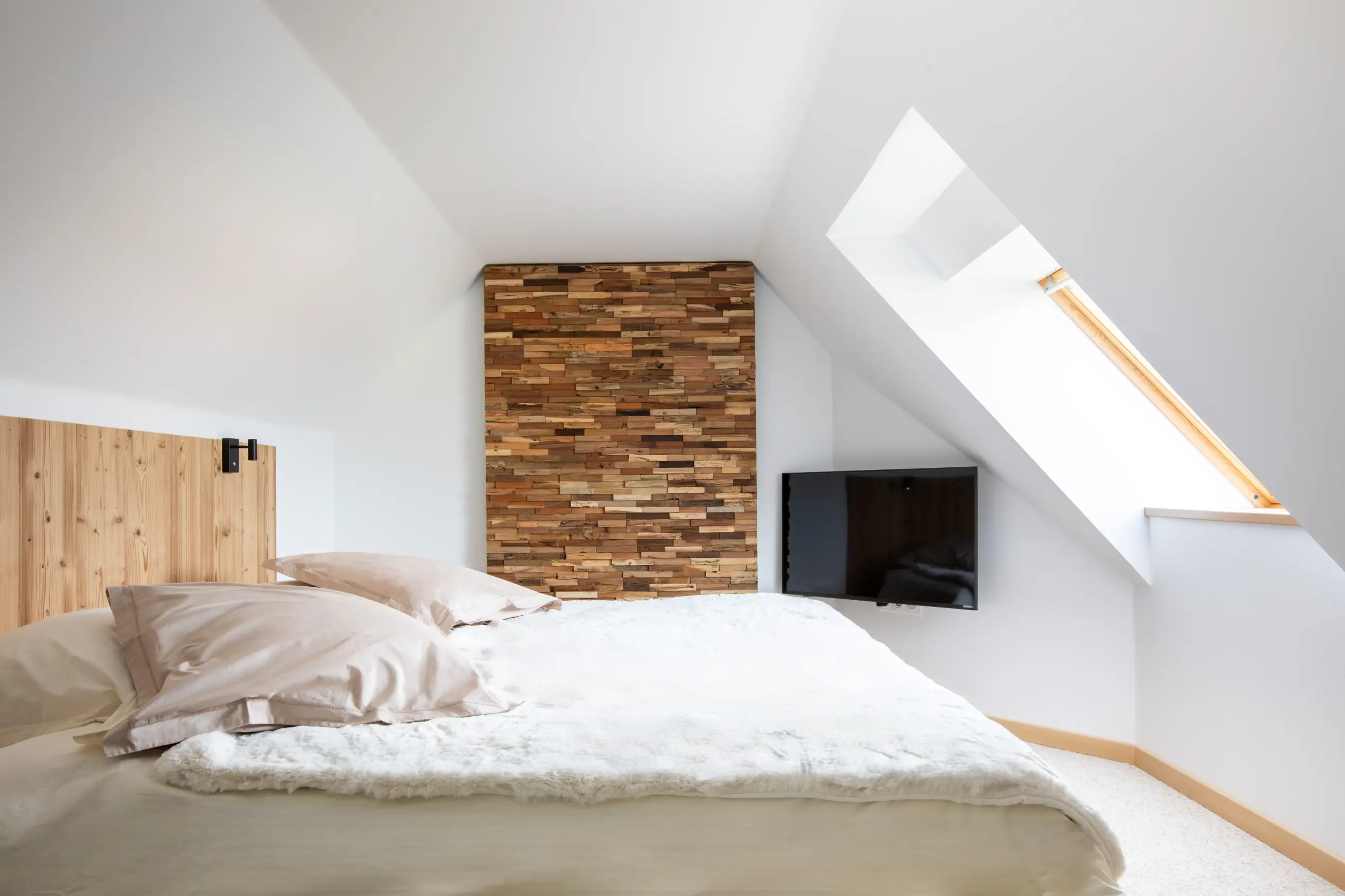 Chambre du gîte Porte D avec lit double, mur en bois décoratif et fenêtre mansardée apportant une belle lumière naturelle.
