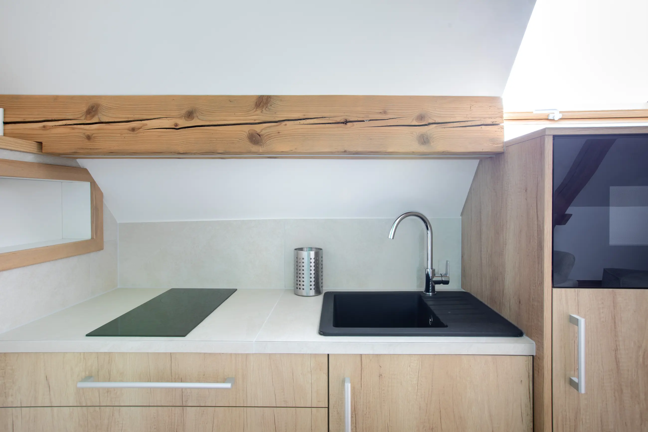 Coin cuisson du gîte Porte D avec plaque de cuisson, évier noir moderne et poutre en bois.