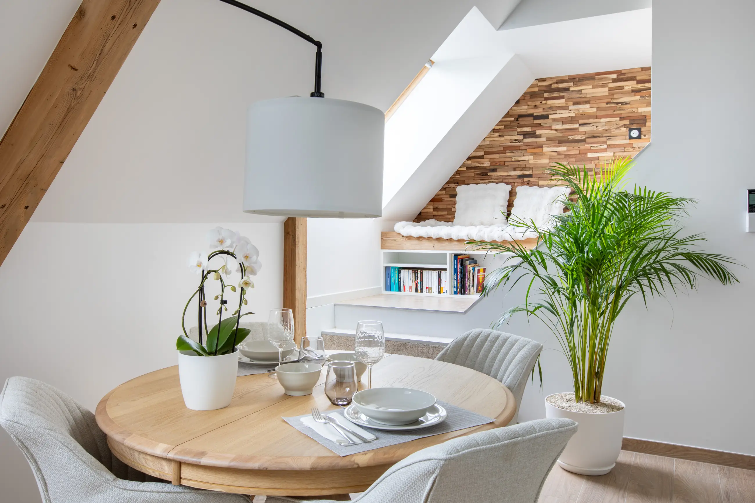 Espace repas du gîte Porte D avec table en bois, chaises confortables et orchidée blanche.