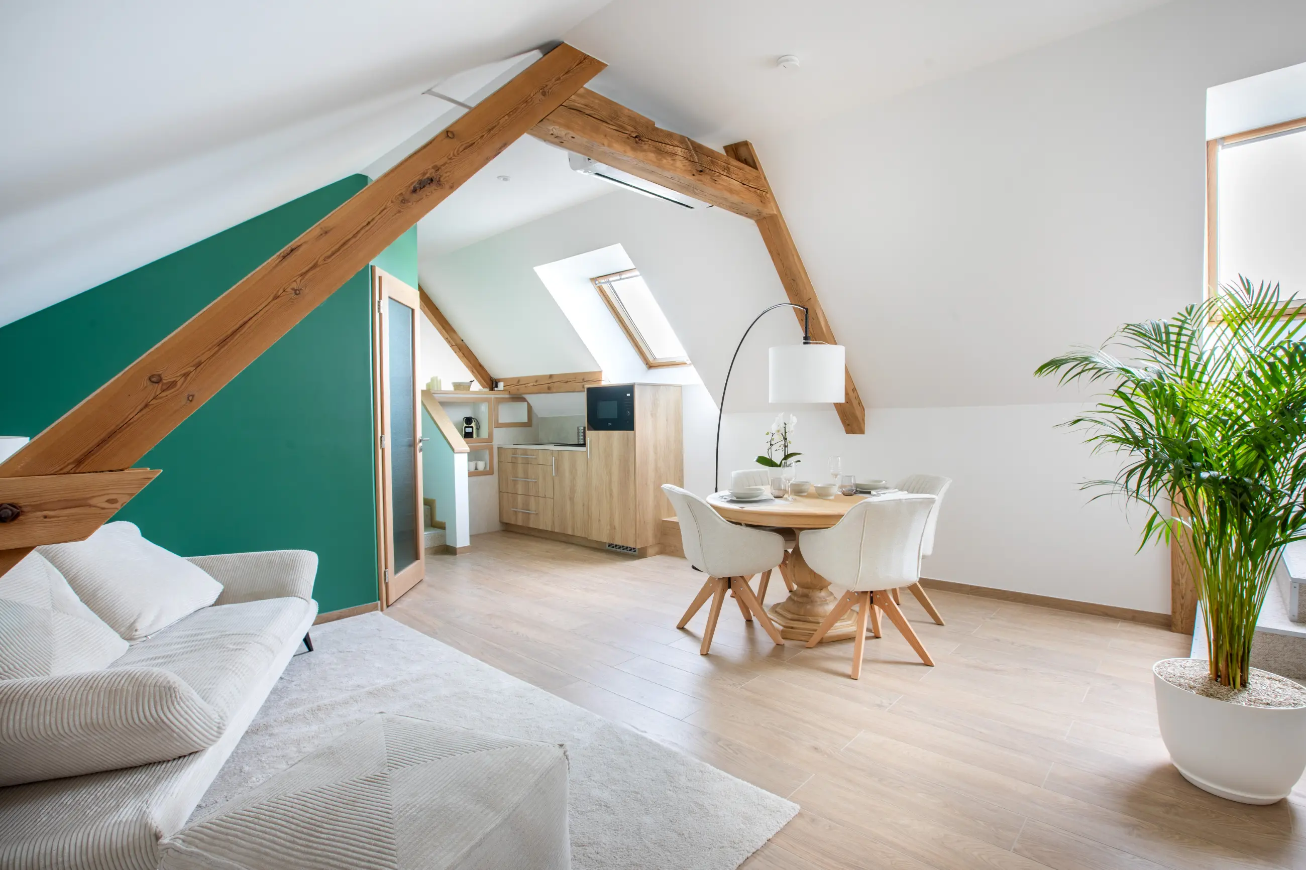 Séjour lumineux du gîte Porte D avec poutres apparentes, canapé clair et coin repas ouvert.